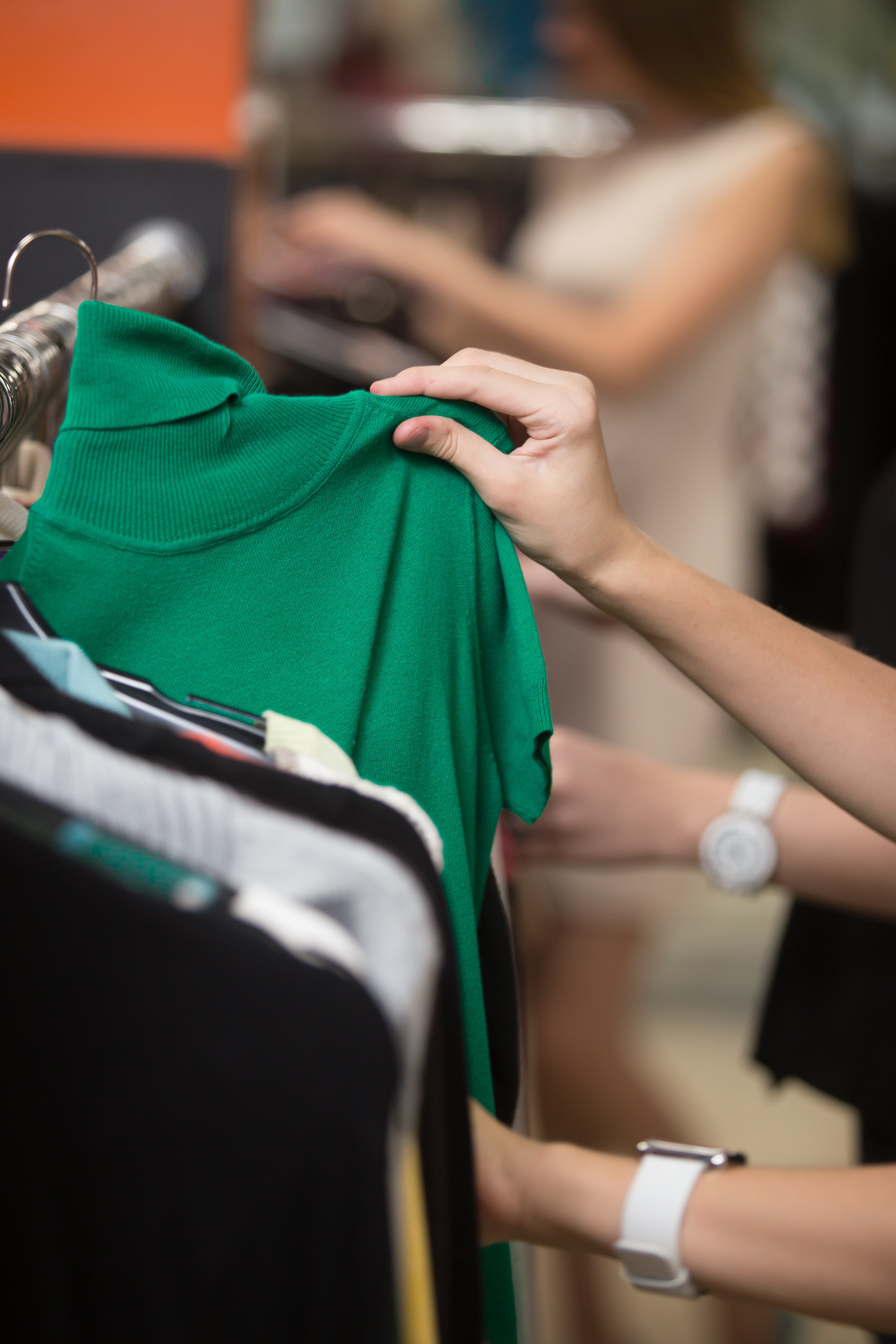 Women shopping in a mall, choosing new clothes, looking through hangers.