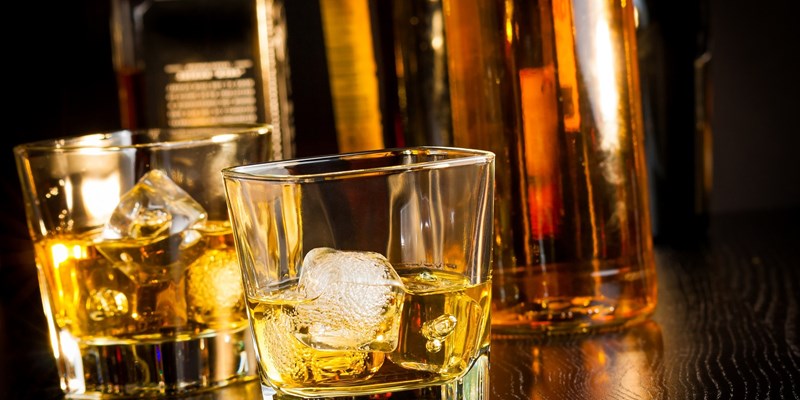 Two glasses of whiskey in front of bottles on wood table