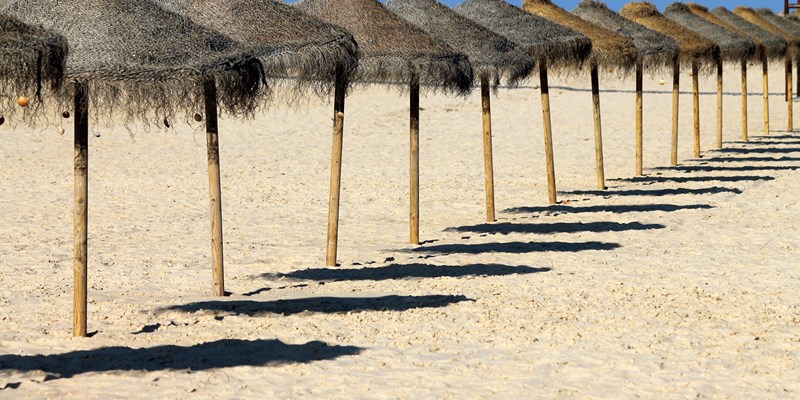 Beach life in the Algarve. Ilha Deserta. The ocean, the beach and an umbrela with seashells.